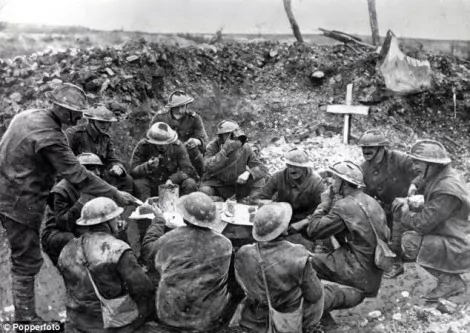 Soldados comendo para celebrar o Natal em uma trincheira parcialmente ocupada pelo túmulo de um companheiro (CRÉDITO: IMPERIAL WAR MUSEUM)